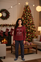 Woman wearing a burgundy long-sleeve top with 'Merry & Bright (and a little tired)' text and plaid pants on a white background.
