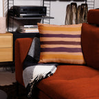 Modern living room with orange sofa, striped designer pillow, and patterned throw. Home decor accents by Design by Lola.